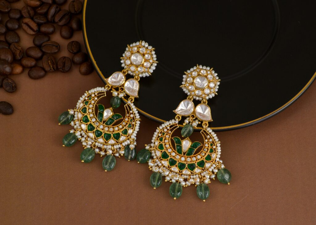 Close-up of ornate beaded earrings with green and gold detailing on a black background.