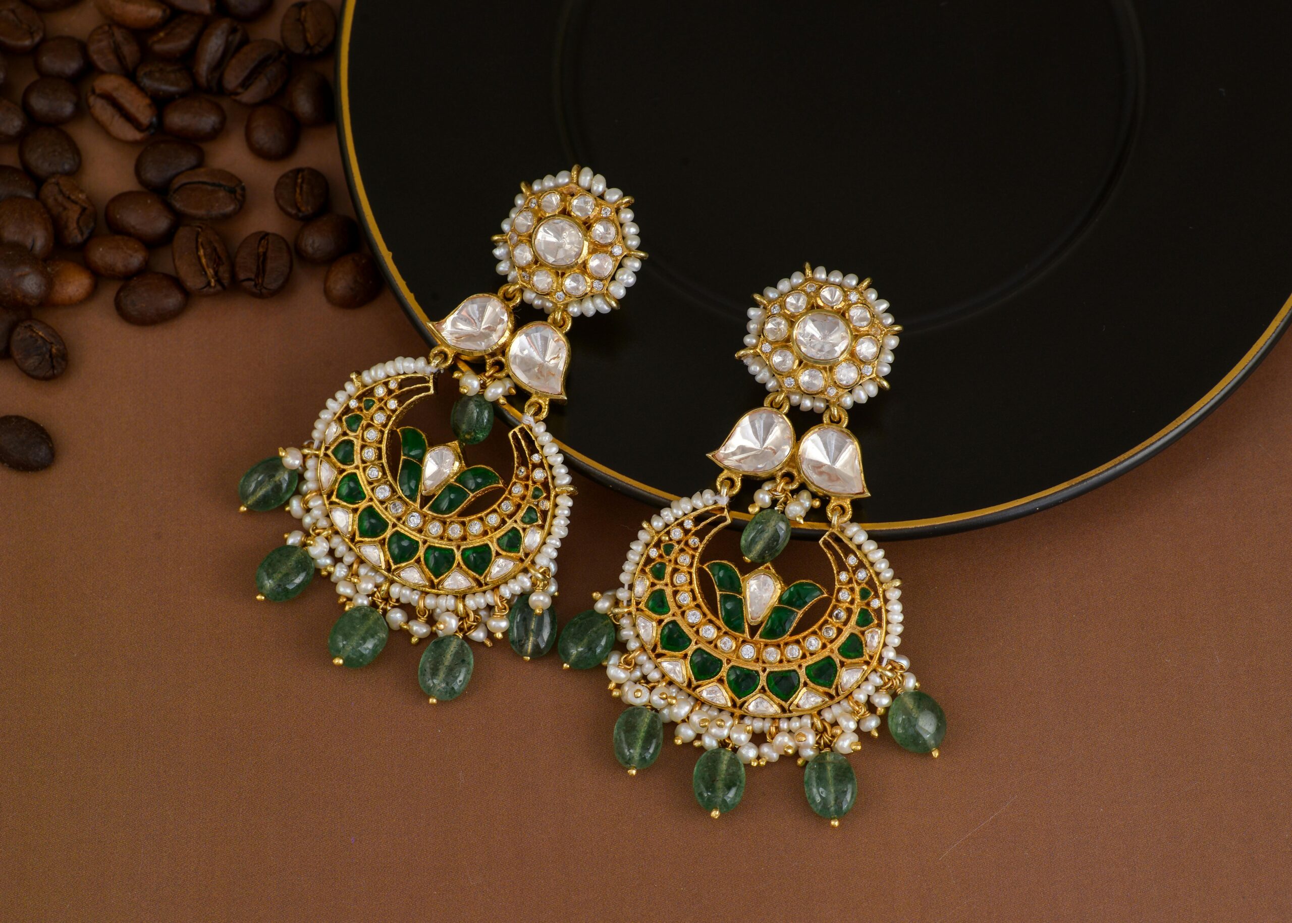 Close-up of ornate beaded earrings with green and gold detailing on a black background.